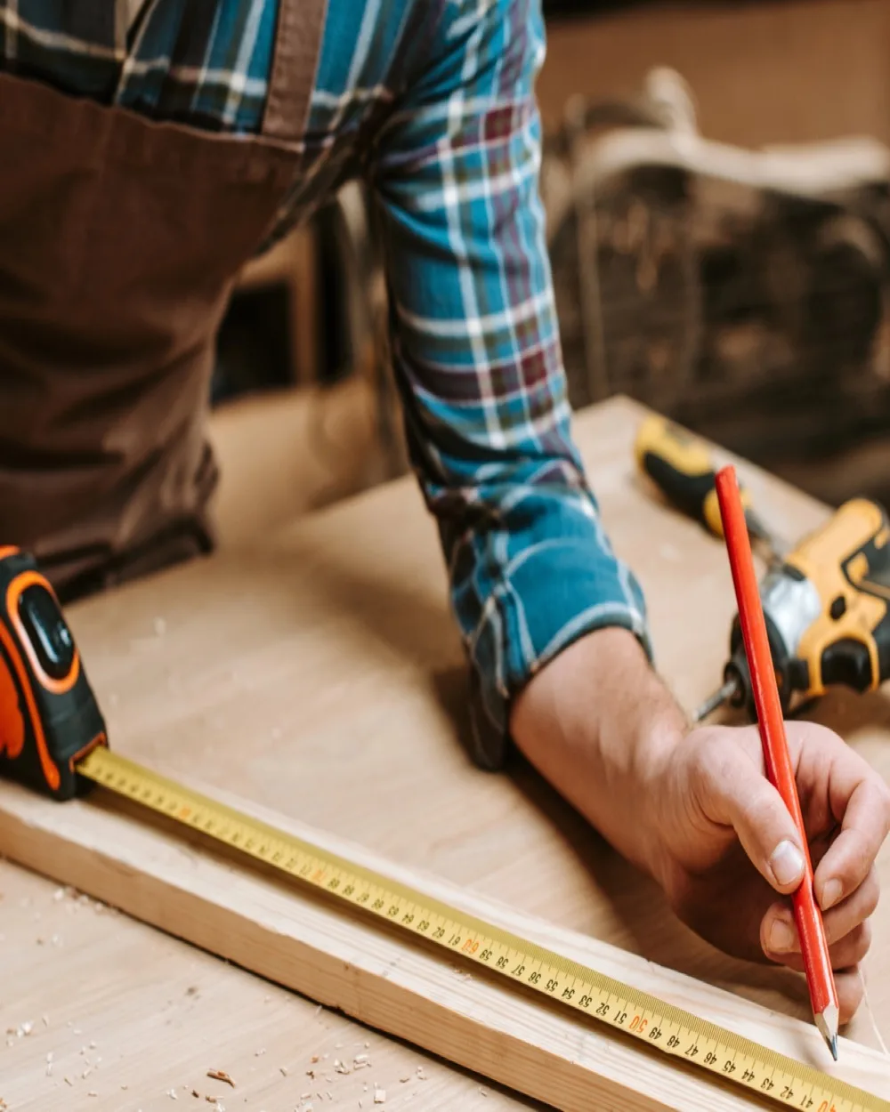 Handwerker misst an der Werkbank ein Brett aus und zeichnet die Schnittkante mit dem Bleistift an